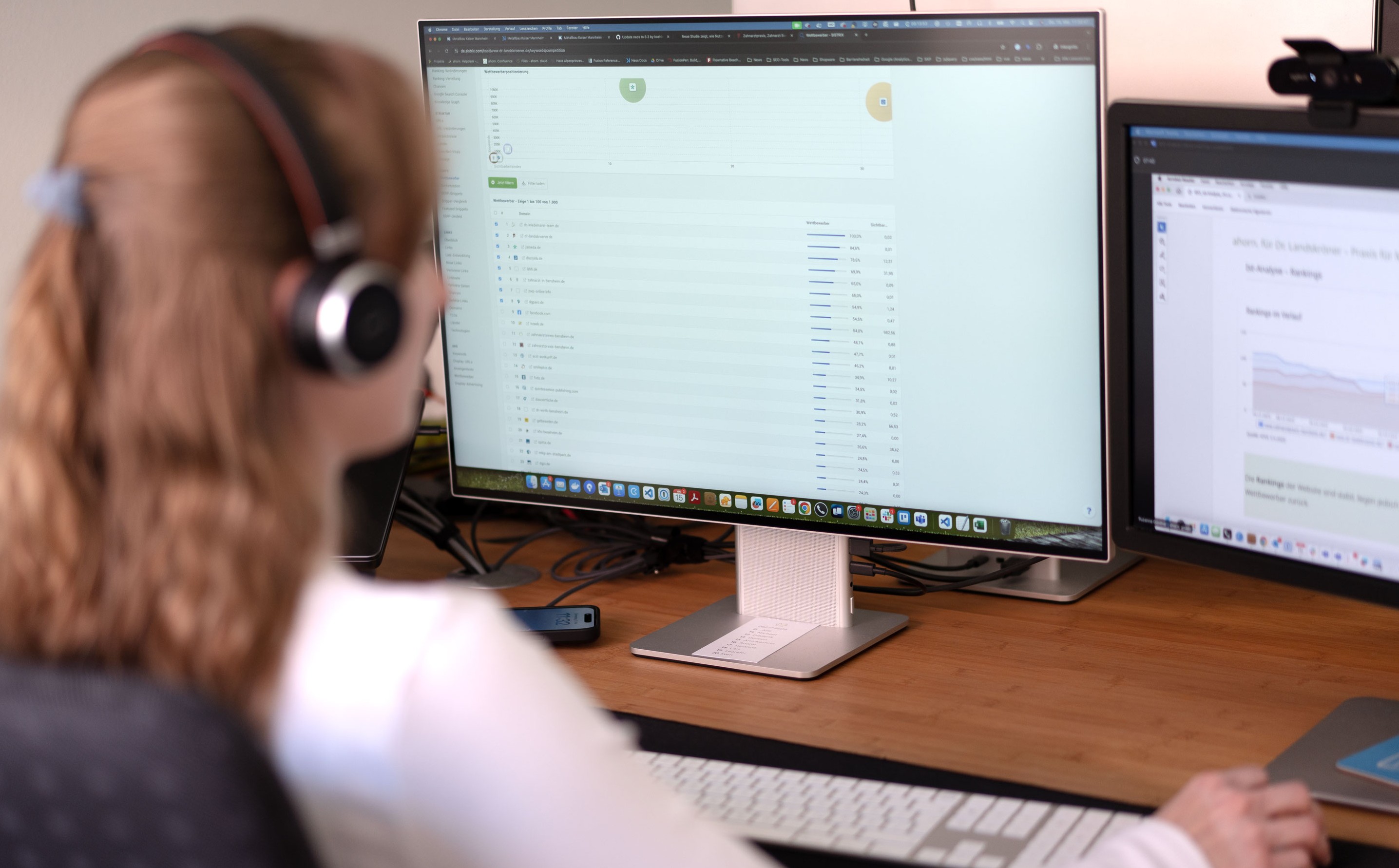 Eine Frau mit Kopfhörern sitzt an einem Schreibtisch mit einem Computer.