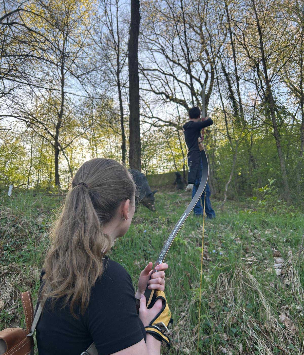 Eine Frau mit einem Bogen und ein Mann stehen im Wald.