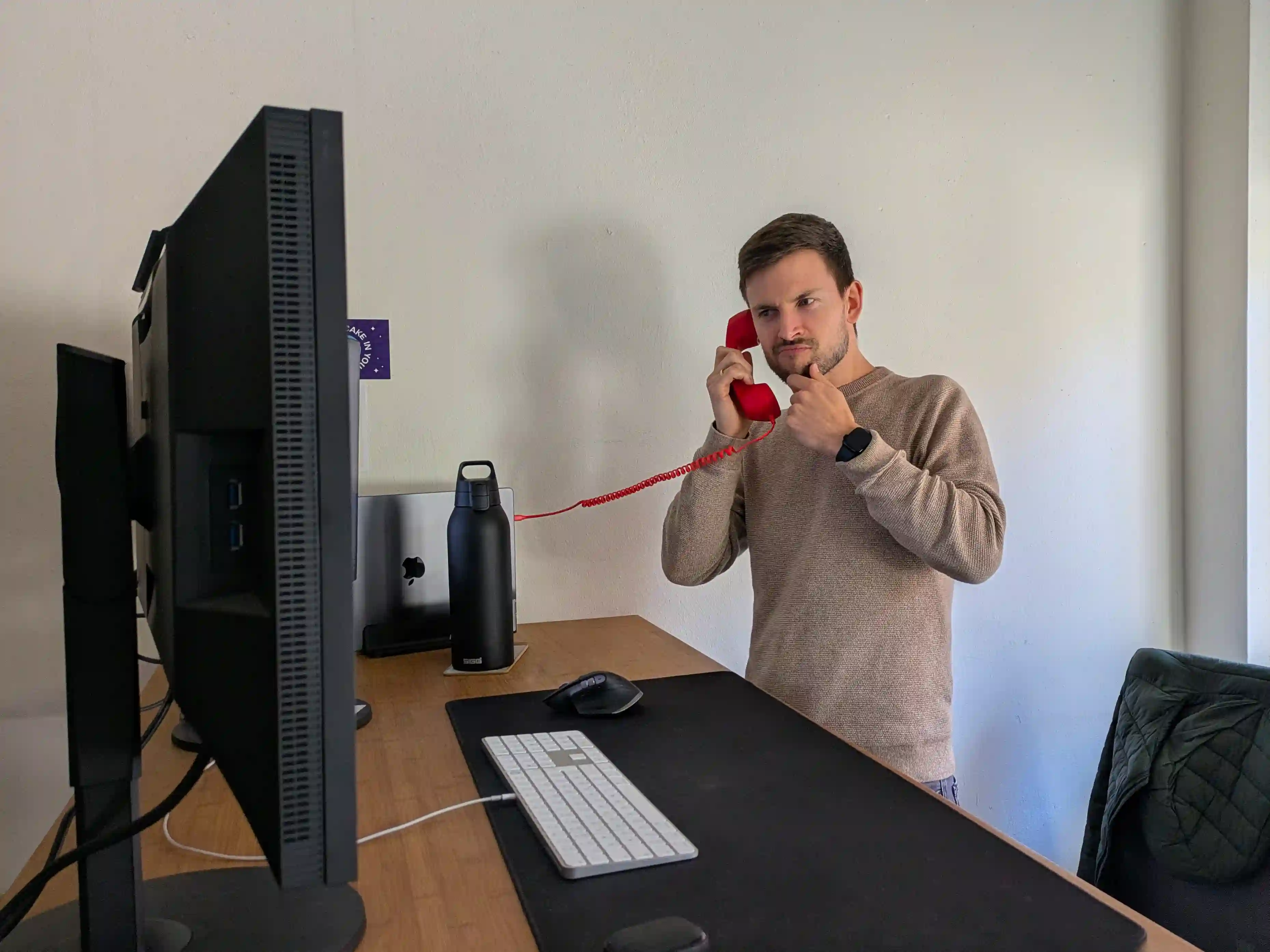 Frederik telefoniert mit einem roten Hörer am Stehschreibtisch und blickt konzentriert auf den Bildschirm