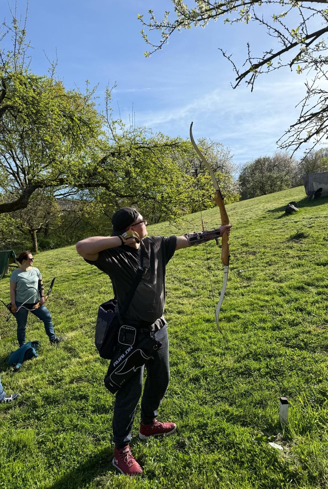 Ein Mann hält Pfeil und Bogen in einem grasbewachsenen Gebiet.