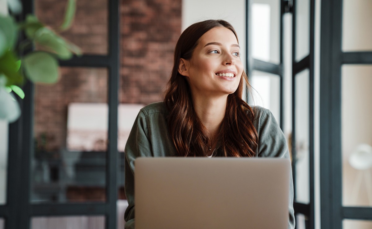 Eine Frau sitzt vor ihrem Laptop und lächelt.